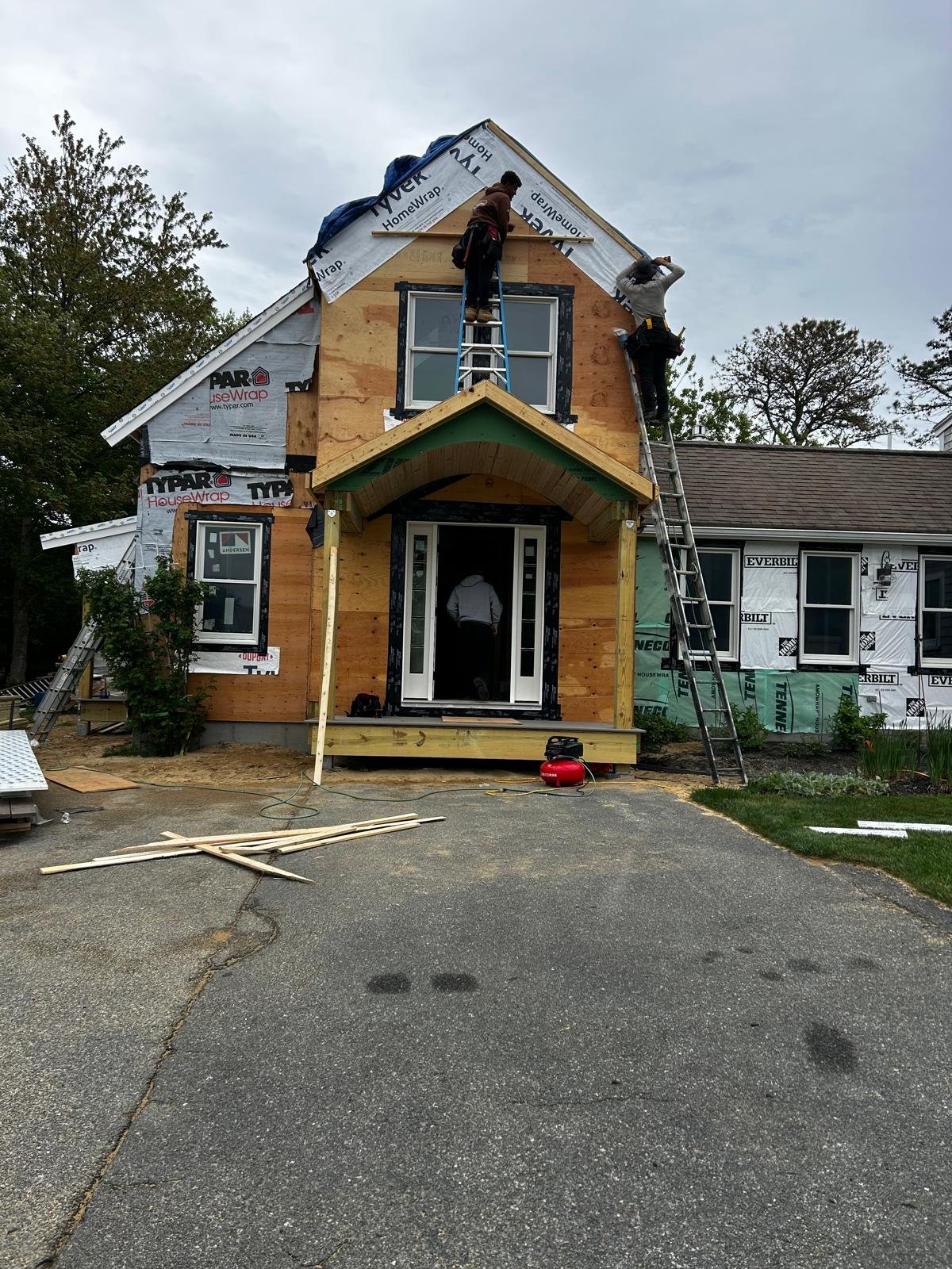 Carpenters on ladders closing in a new dormer, housewrap exposed on the second floor